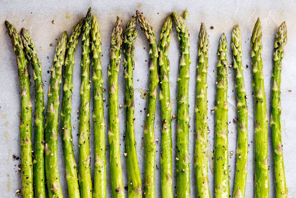 4.	Den grünen Spargel sorgfältig waschen, die holzigen Enden abschneiden und die Spargelstangen nebeneinander auf dem zweiten Backblech ausbreiten. Mit Olivenöl beträufeln. 