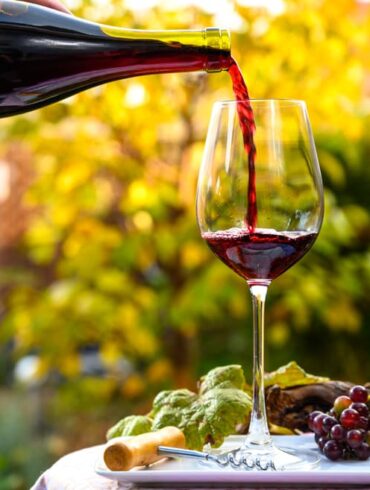 Glas steht auf Tisch im Garten und wird mit Rotwein befüllt.