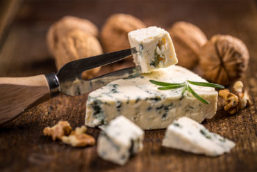Angeschnittener Blauschimmelkäse vor Walnüssen