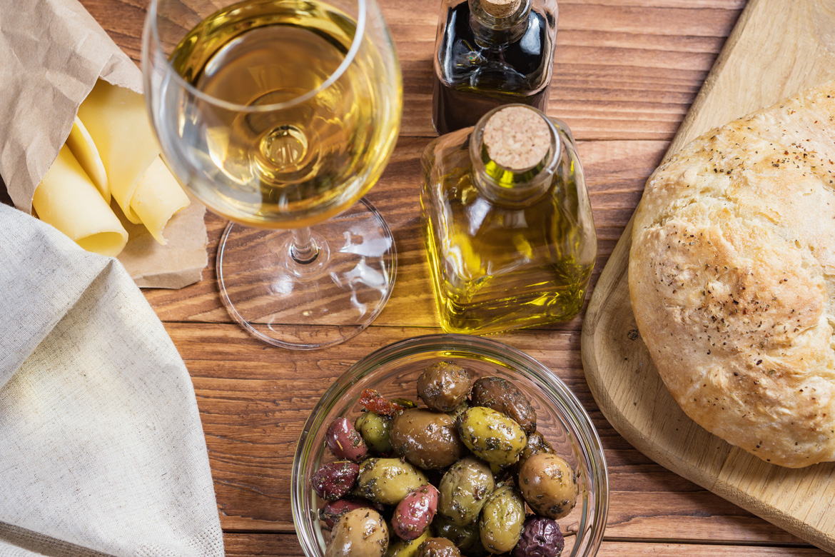 Weißwein, Öl, Oliven, Brot auf Holztisch