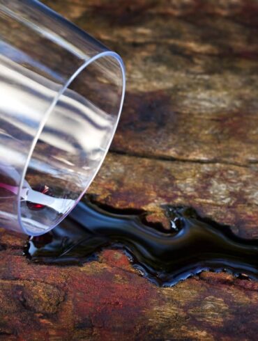 Aus umgefallen Glas läuft Rotwein auf Holztisch