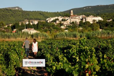 rhone logo 2 Zwei Personen laufen durch einen Weinberg zwischen Reben in der Rhône untern rechts eingefügtes Logo der Côtes du Rhône