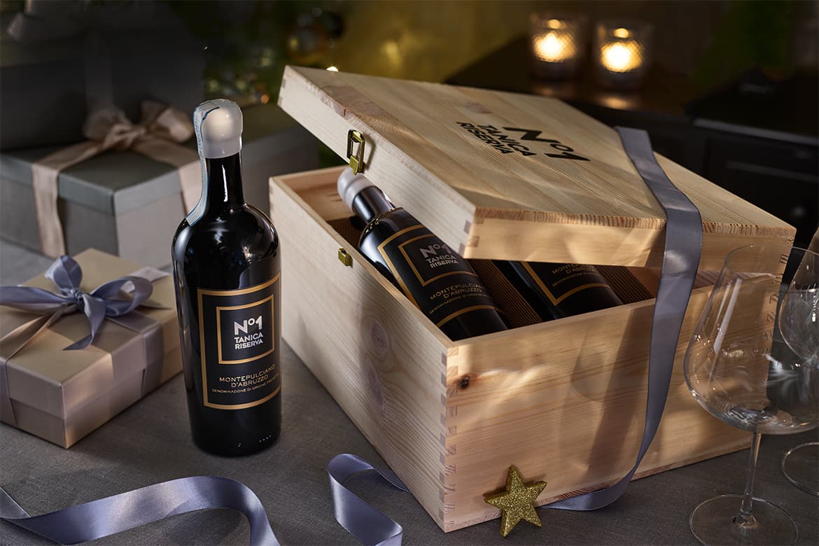 Wein in Holzkisten edel verpackt, darum liegen einige Geschenke, sowie ein Weinglas und Kerzen