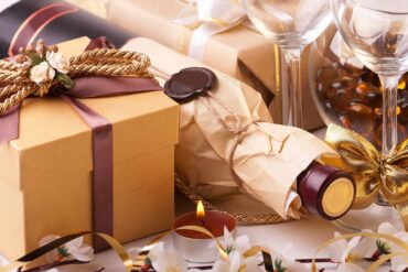 weine verschenken Weinflasche in Geschenkpapier verpackt, daneben ein Geschenk und ein Weinglas