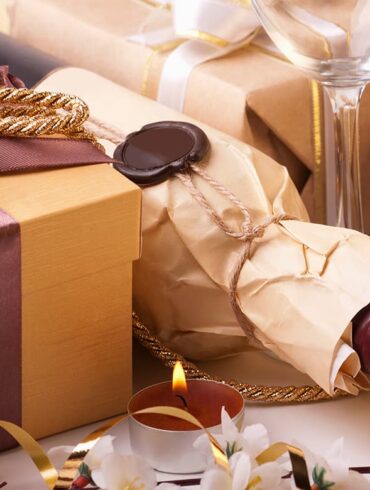 Weinflasche in Geschenkpapier verpackt, daneben ein Geschenk und ein Weinglas