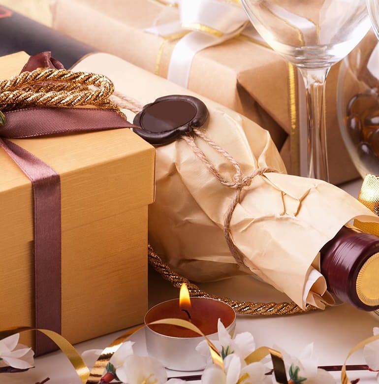 Weinflasche in Geschenkpapier verpackt, daneben ein Geschenk und ein Weinglas