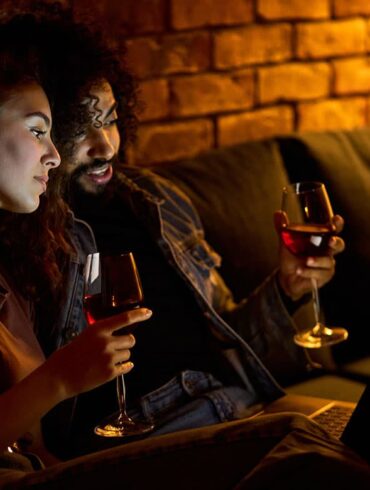 Zwei Menschen schauen einen Film auf einem Laptop und trinken Wein