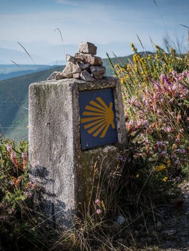 Meilenstein, auf dem das Zeichen des Jakobsweges ist, im Hintergrund Berglandschaft