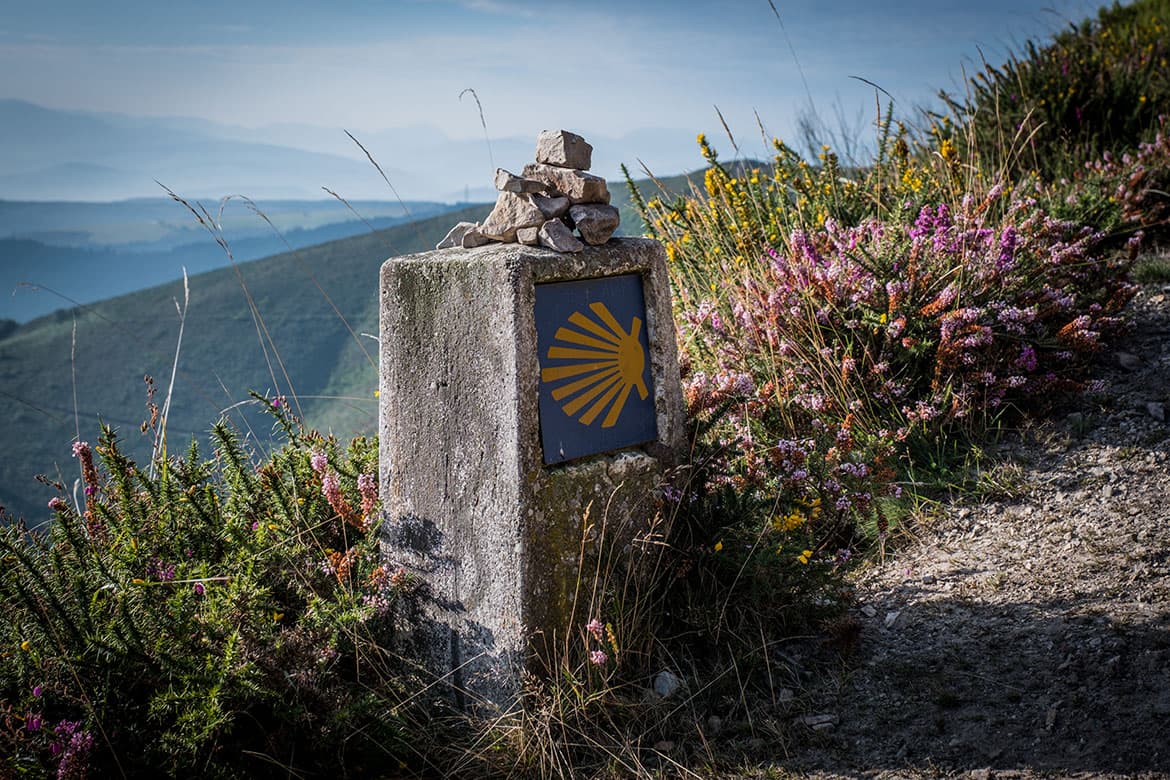 Meilenstein, auf dem das Zeichen des Jakobsweges ist, im Hintergrund Berglandschaft