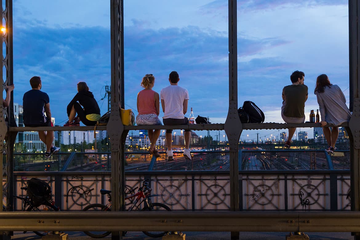 Personen sitzen auf einer Brücke und genießen den Sonnenuntergang über München